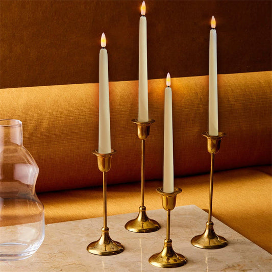 Gold candle holders with white candles on a marble surface against a warm-toned wall.