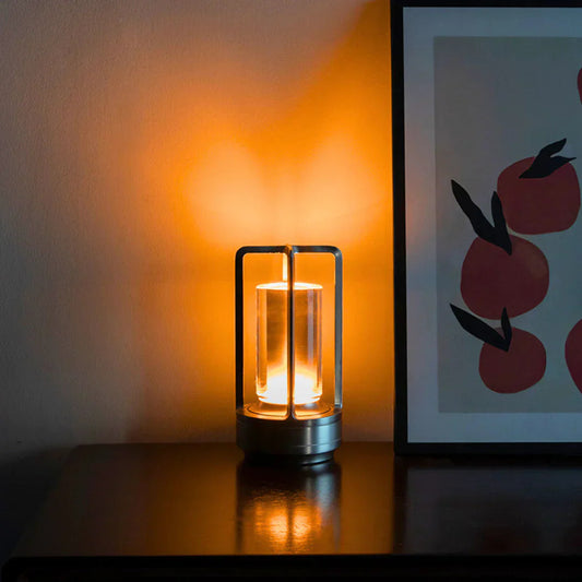 Small lamp with warm glow on a surface next to a framed picture of apples.