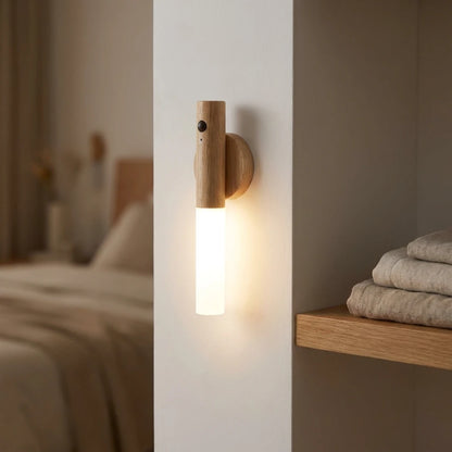 Josh & Tate - LumiDock™ Motion Wall Light - Wooden wall sconce emitting light in a bedroom setting with a bed and shelf in the background.