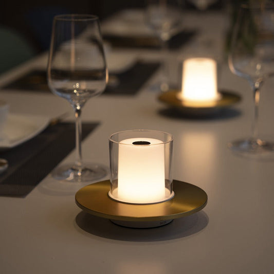 Decorative candle in a glass holder on a table with wine glasses and plates.