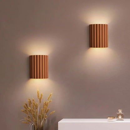 Two cylindrical wall lights on a neutral wall with decorative elements.