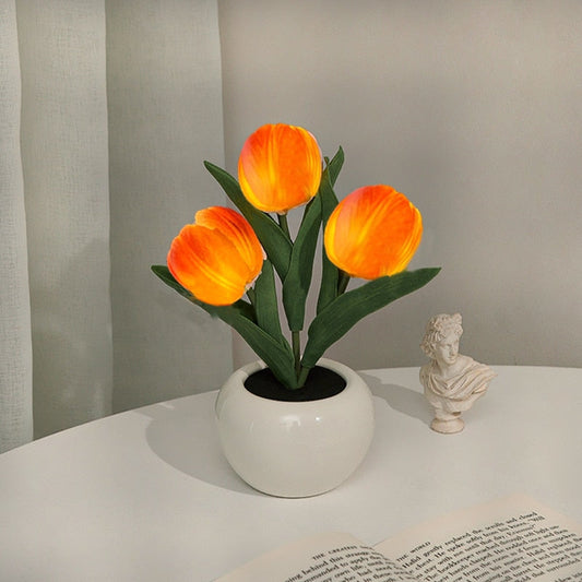 Artificial orange tulips in a white pot on a table with a gray curtain background