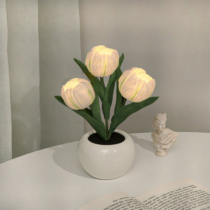 Decorative potted plant with illuminated bulbs on a table next to a classical statue.