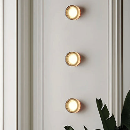 Three round wall lights on a light gray wall with a plant in the corner.