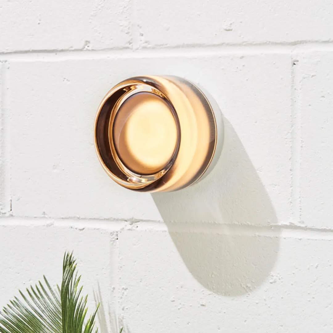 Wall-mounted outdoor light fixture on a white brick wall with a plant in the foreground.