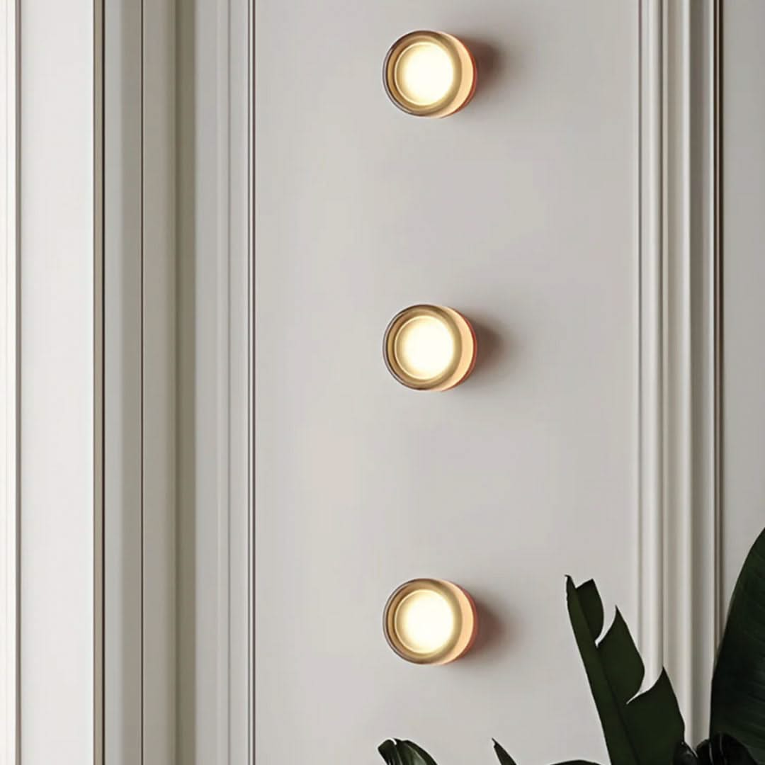 Three round wall lights on a light gray wall with a plant in the corner.