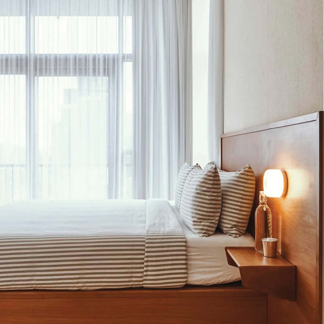 Bedroom with wooden bed, striped bedding, and a nightstand with a lamp.