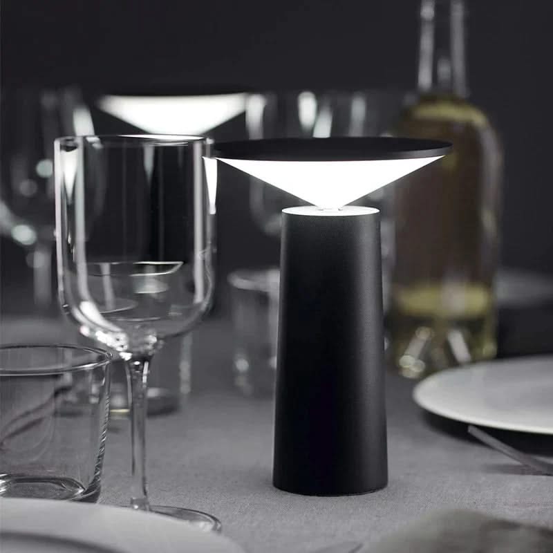 Modern black table lamp on a dining table with wine glasses and plates.