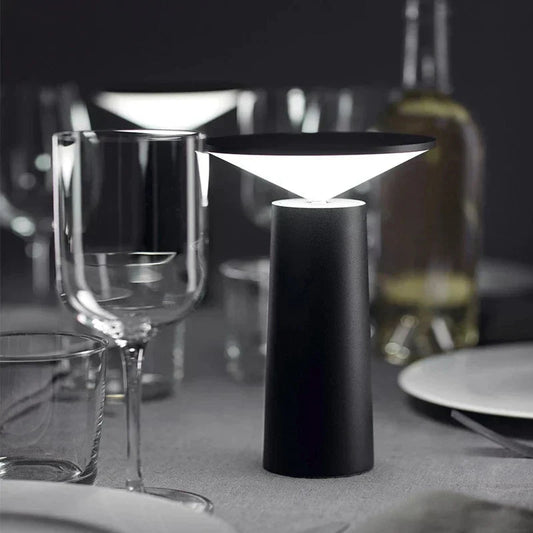Modern black table lamp on a dining table with wine glasses and plates.