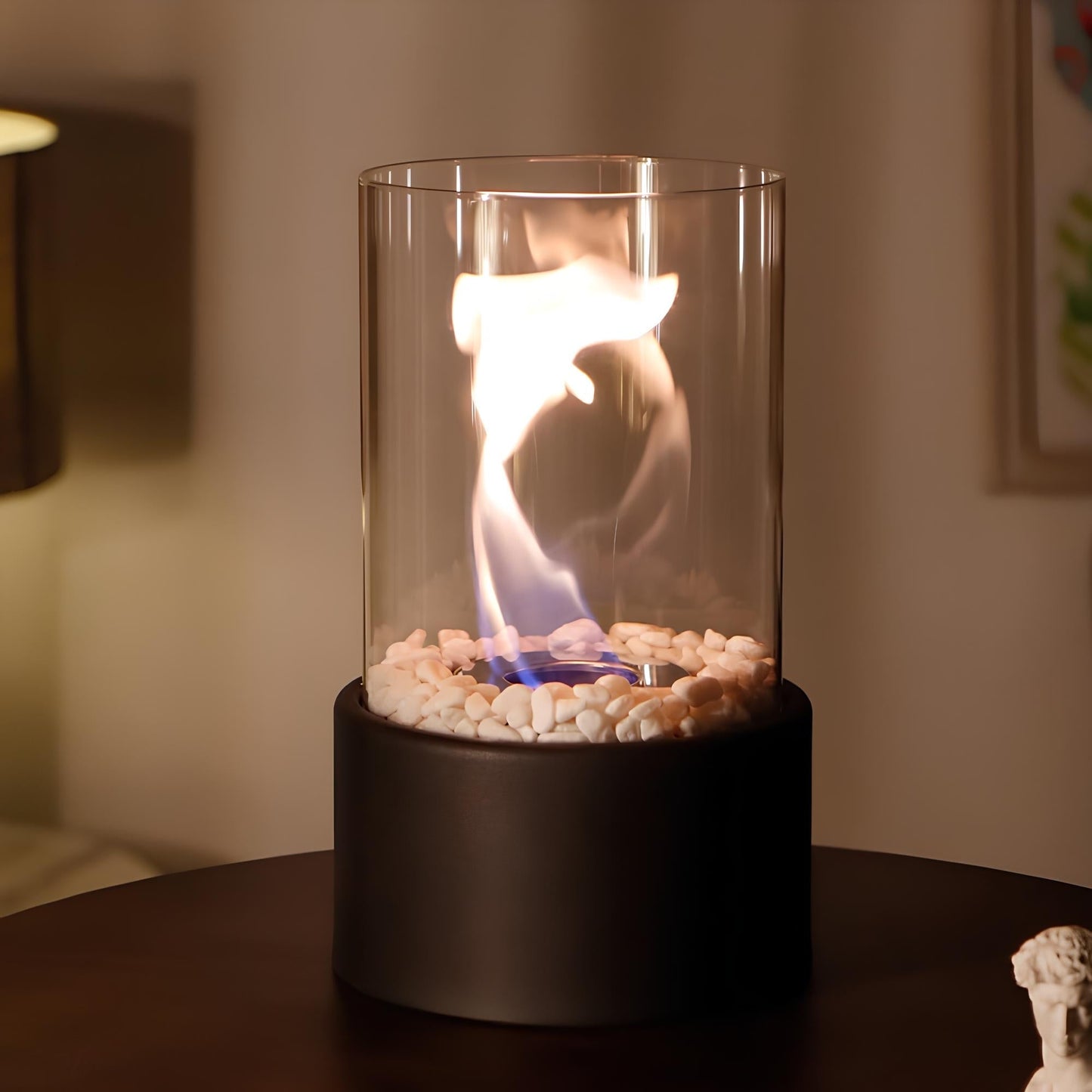 Tabletop fire pit with flames inside a glass container on a dark surface.