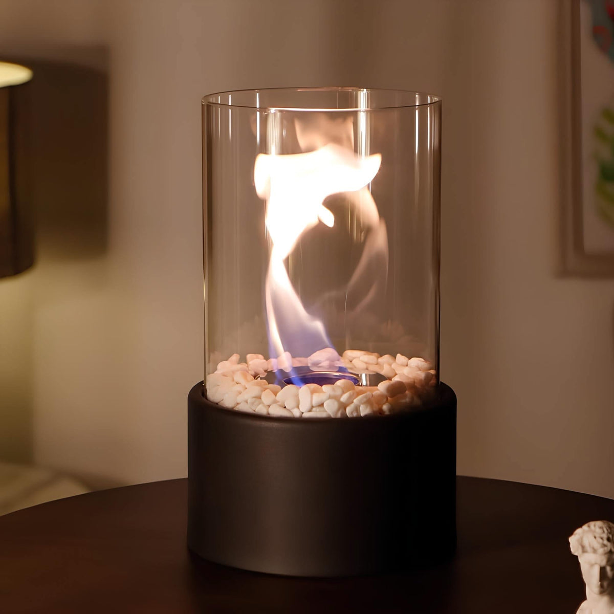 Tabletop fire pit with flames inside a glass container on a dark surface.