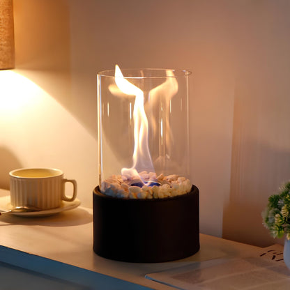 Small table top fireplace with glass cover on a desk next to a cup and plant.
