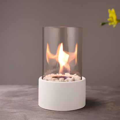 Small portable fireplace with glass cover on a gray surface, featuring a yellow flower in the corner.