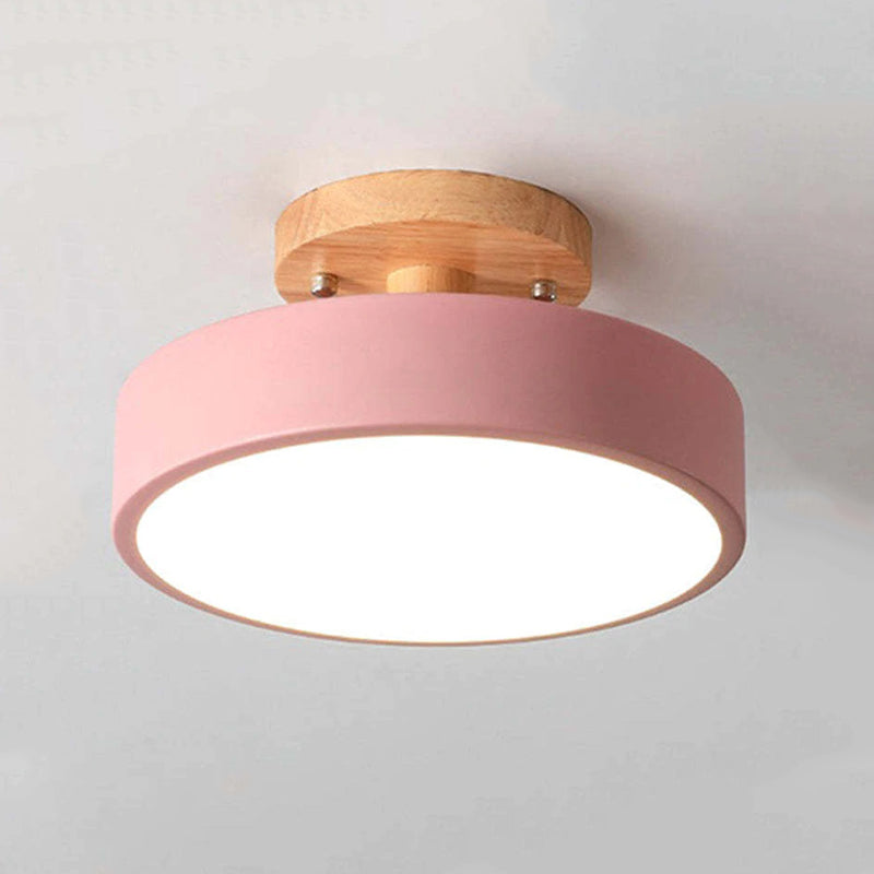 Ceiling light fixture with pink shade and wooden fixture on a plain background