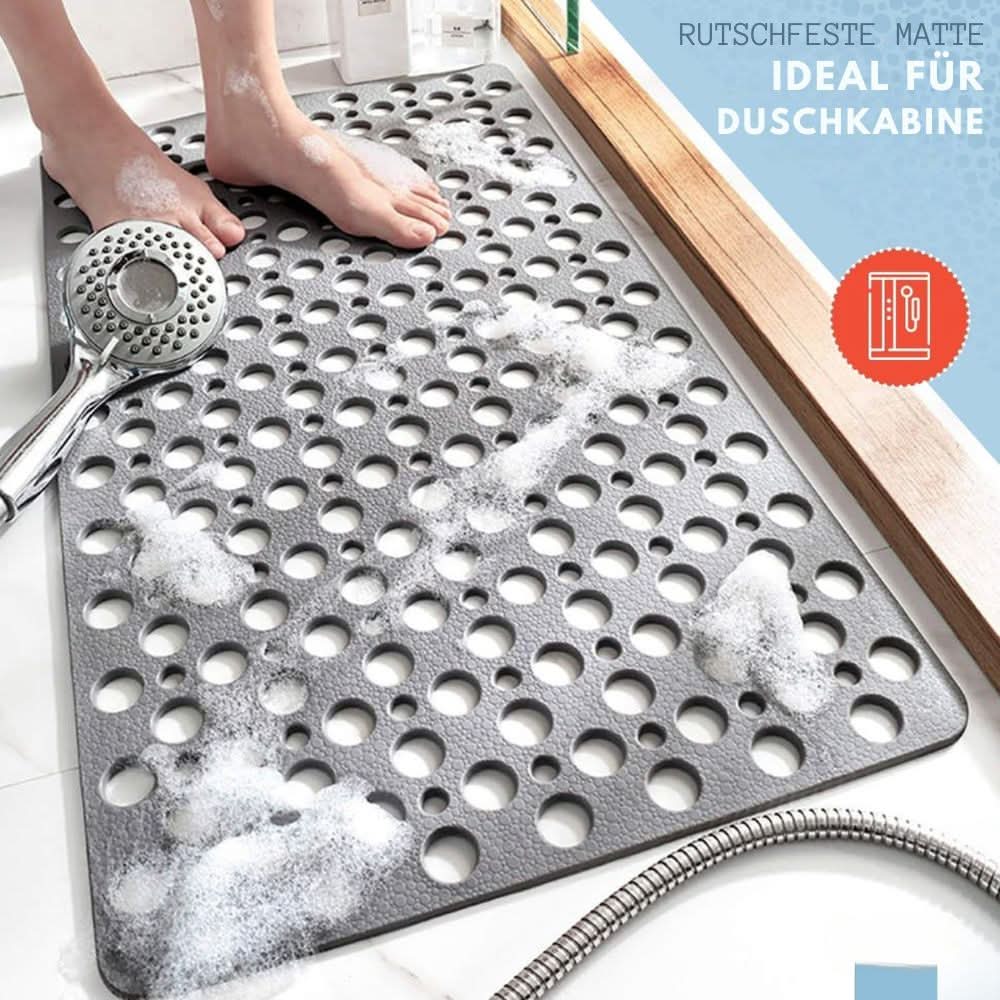 Gray textured mat with holes on a bathroom floor, showing feet stepping onto it.