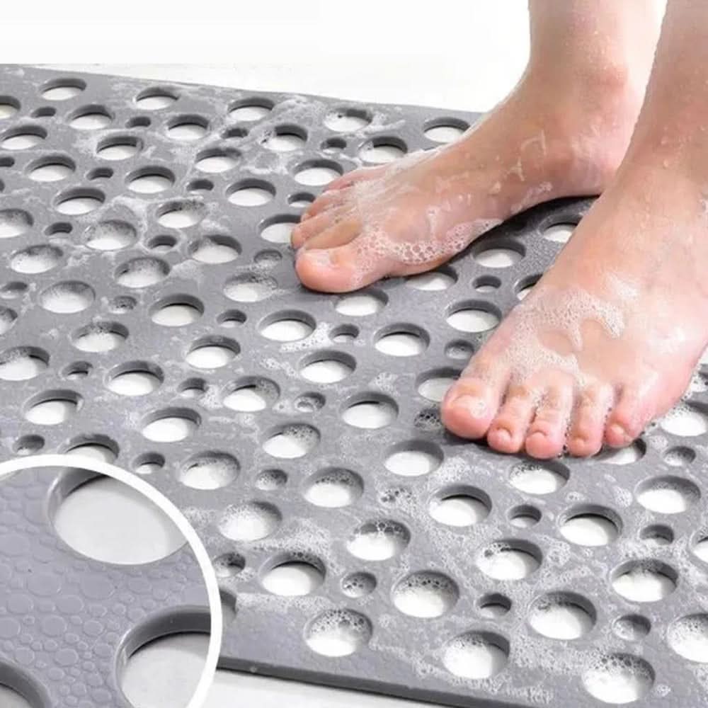 Person standing on a textured gray mat with holes, feet covered in soap suds.