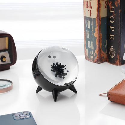 Decorative black and clear sphere on a white surface with books and a magnifying glass in the background.
