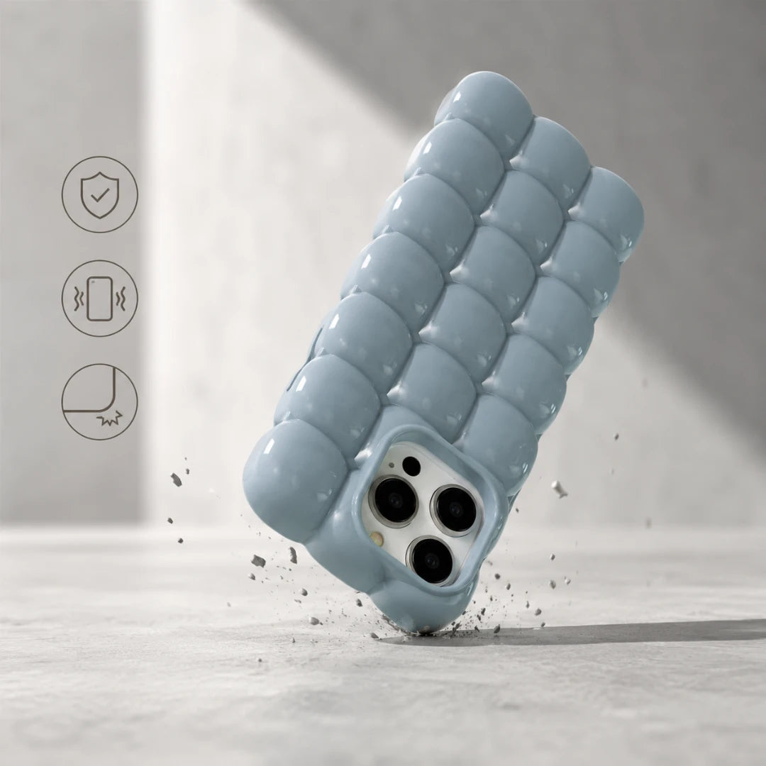 Josh & Tate - MarshBubble™ Puffy iPhone Case - A light blue textured phone case with a wavy, segmented bubble design, shown floating at an angle on a light gray surface with small debris around it. Three thin black feature icons appear on the left side of the image.