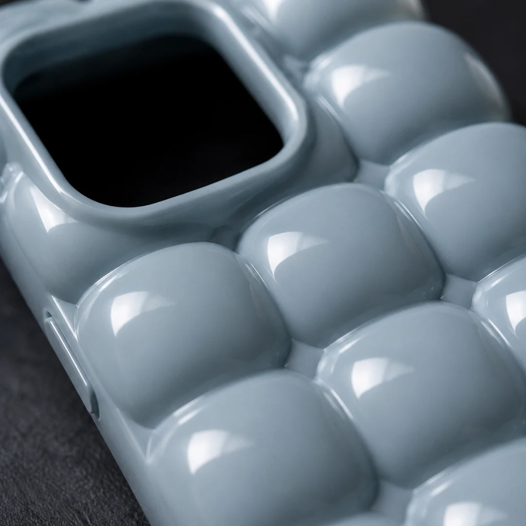 Josh & Tate - MarshBubble™ Puffy iPhone Case - A close-up of a glossy, light blue phone case featuring a raised, bubble-like segmented pattern and a square camera cutout.