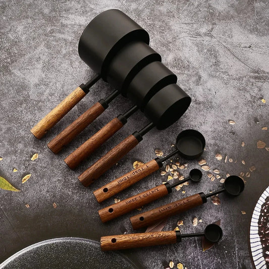 Josh & Tate - Measuring Spoon Set (Wood Handle) - Set of black and wooden measuring spoons on a textured surface with oats.