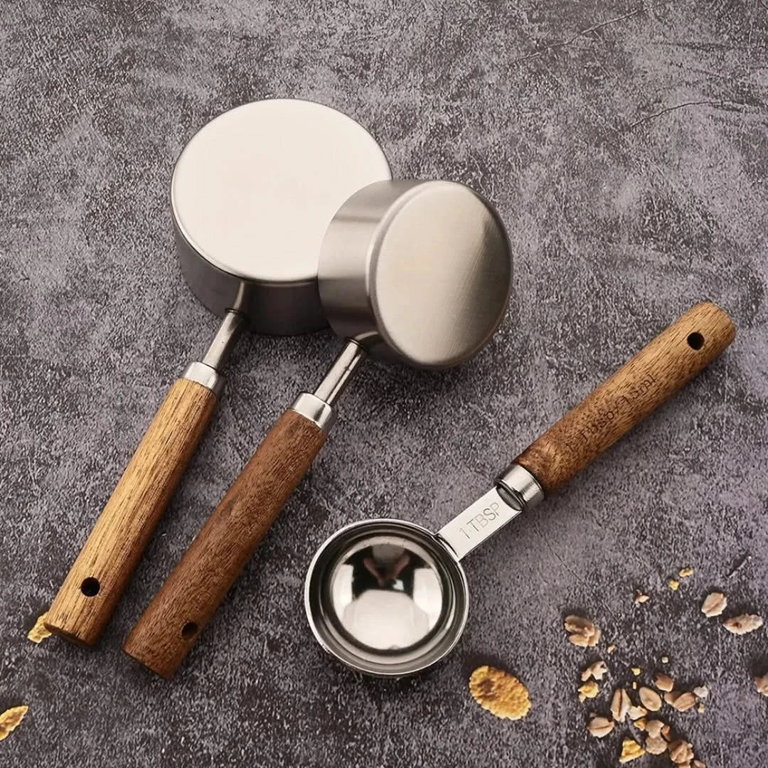 Josh & Tate - Measuring Spoon Set (Wood Handle) - Three metal measuring cups with wooden handles on a gray surface.