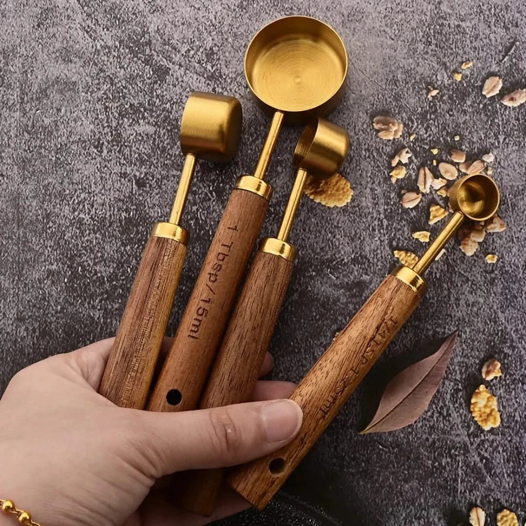 Josh & Tate - Measuring Spoon Set (Wood Handle) - Set of wooden measuring spoons with gold accents held by a hand on a textured surface.