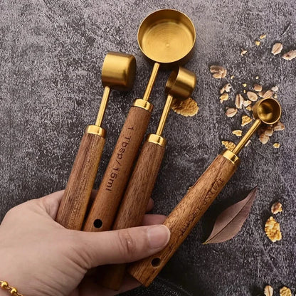 Josh & Tate - Measuring Spoon Set (Wood Handle) - Set of wooden measuring spoons with gold accents held by a hand on a textured surface.