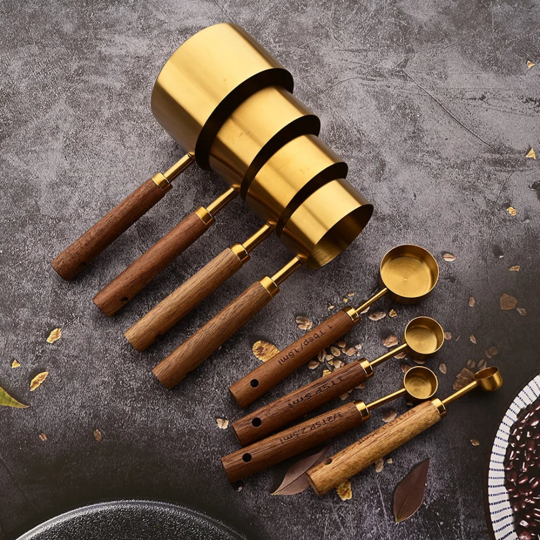 Set of gold and wooden measuring cups and spoons on a dark surface with coffee beans.