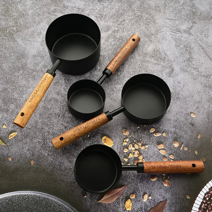 Set of black measuring cups with wooden handles on a gray surface.