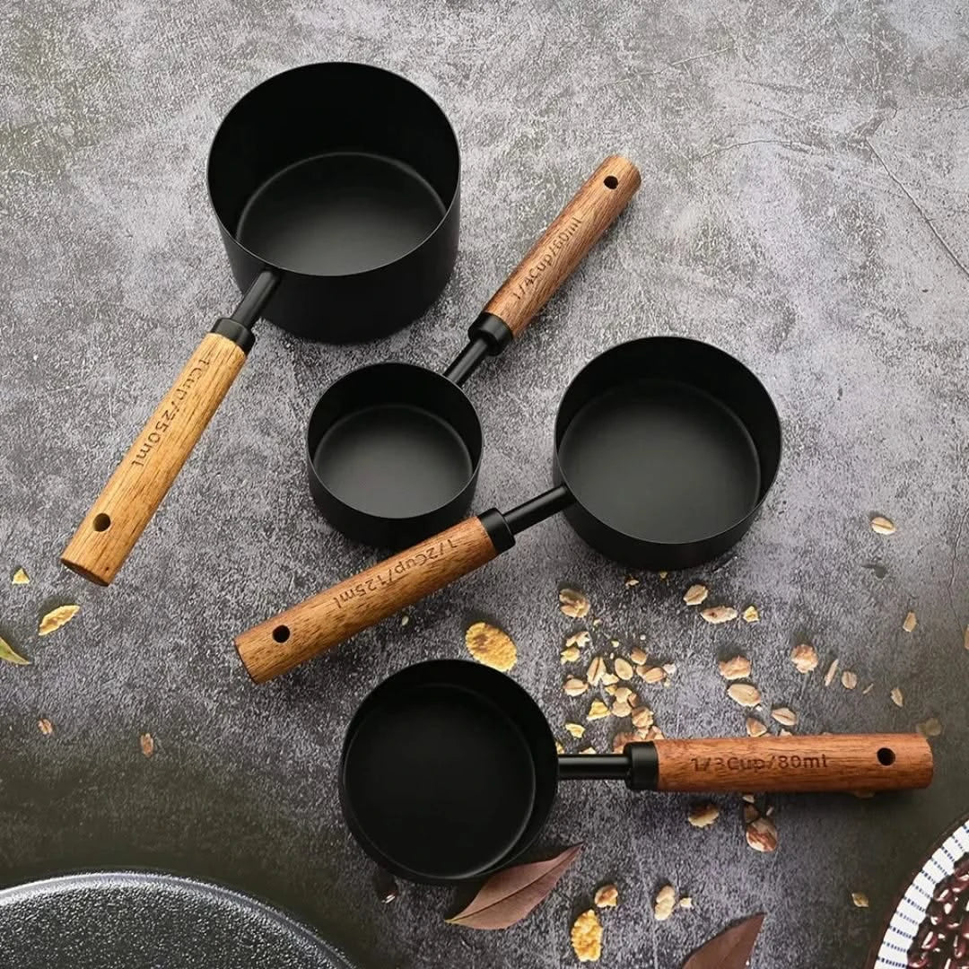 Josh & Tate - Measuring Spoon Set (Wood Handle) - Set of black measuring cups with wooden handles on a gray surface with scattered leaves.