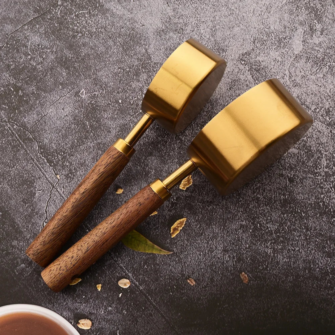 Two brass mallets with wooden handles on a dark surface with coffee beans.