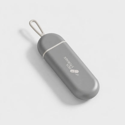 Josh & Tate - MedicineStorage™ Portable Pill Organizer - A gray pill-shaped portable storage case with a white loop strap and white logo text reading 'BOX STORAGE' on a light gray background.