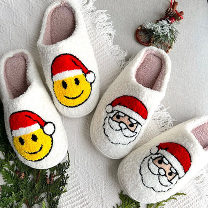Pair of white slippers with Santa Claus and smiley face designs on a textured surface.