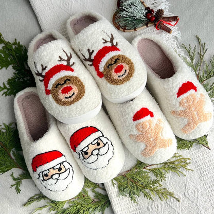 Set of Christmas-themed slippers with Santa and reindeer designs on a white surface with greenery.