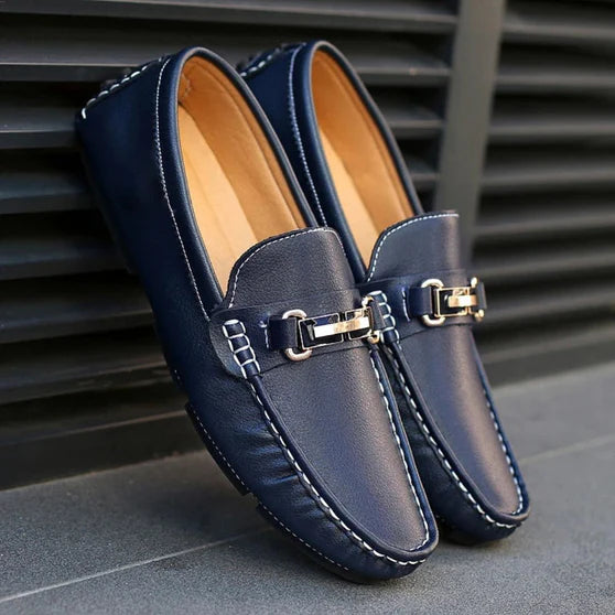 A pair of black Milano Classic Loafers with a sleek metal buckle on a city sidewalk.