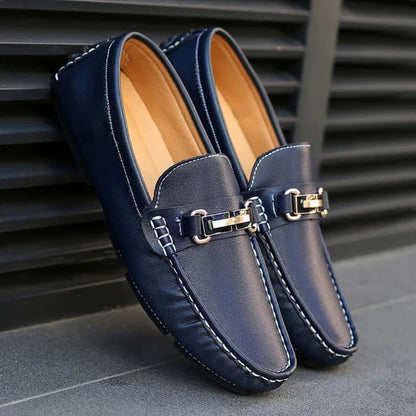 A pair of black Milano Classic Loafers with a sleek metal buckle on a city sidewalk.