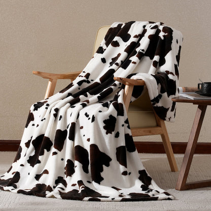 Cow print blanket draped over a wooden chair against a beige wall.