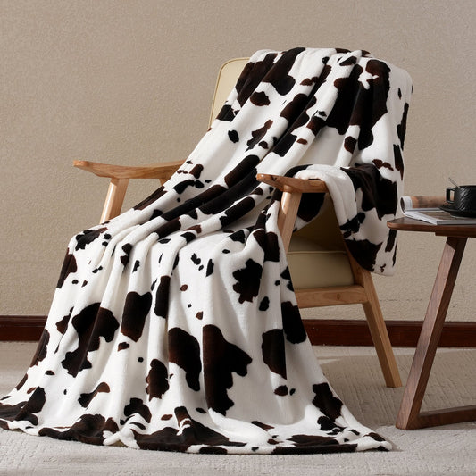 Cow print blanket draped over a wooden chair against a beige wall.