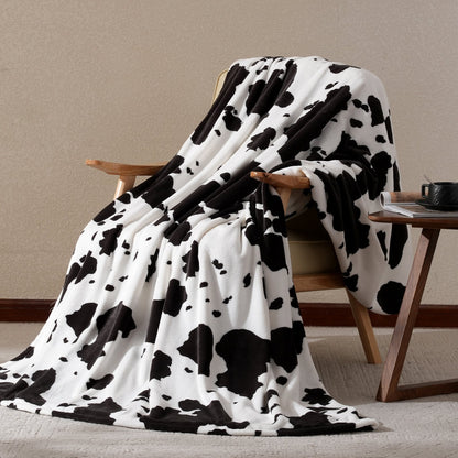 Black and white cow print blanket draped over a wooden chair against a beige wall.