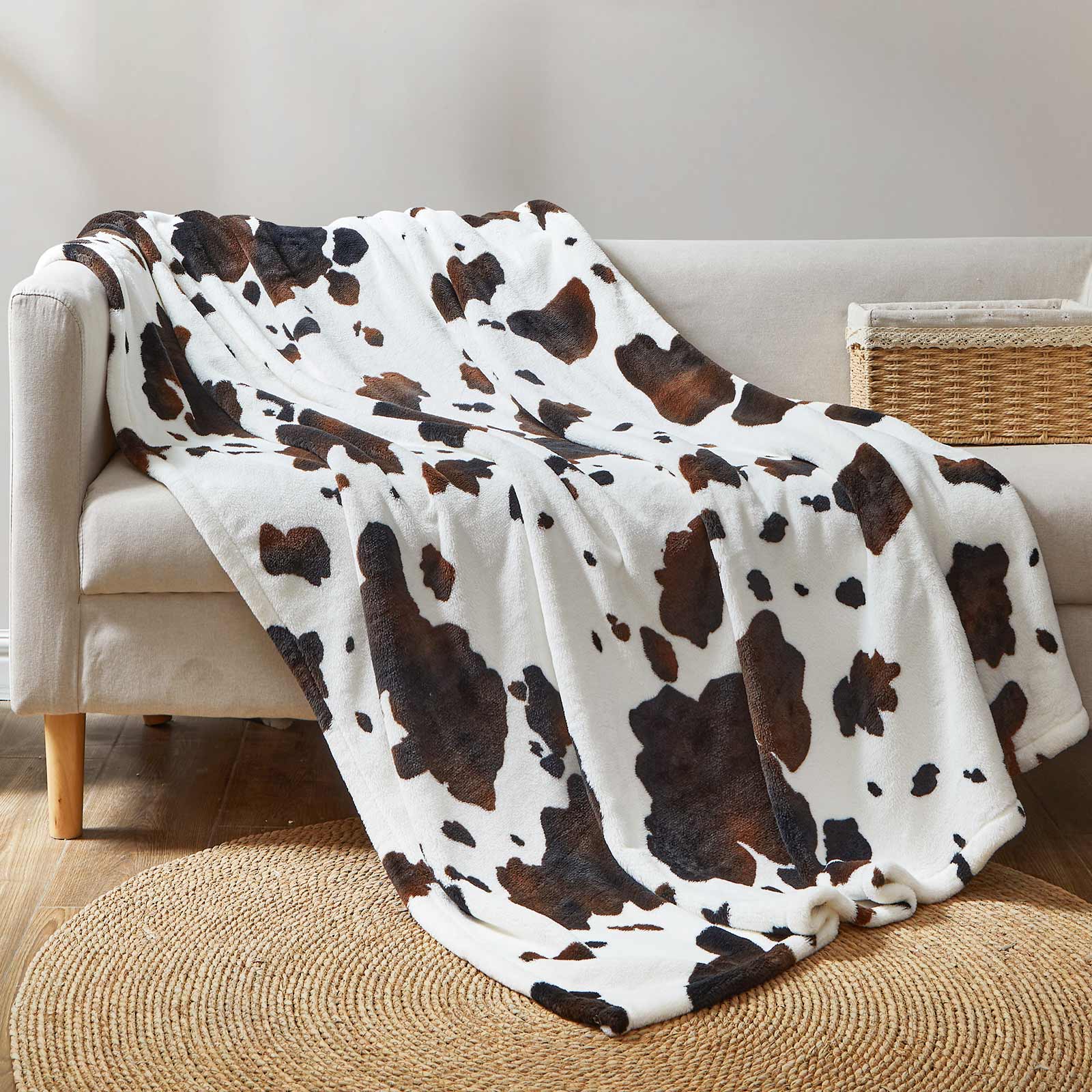 Cow print blanket draped over a beige sofa in a living room setting.