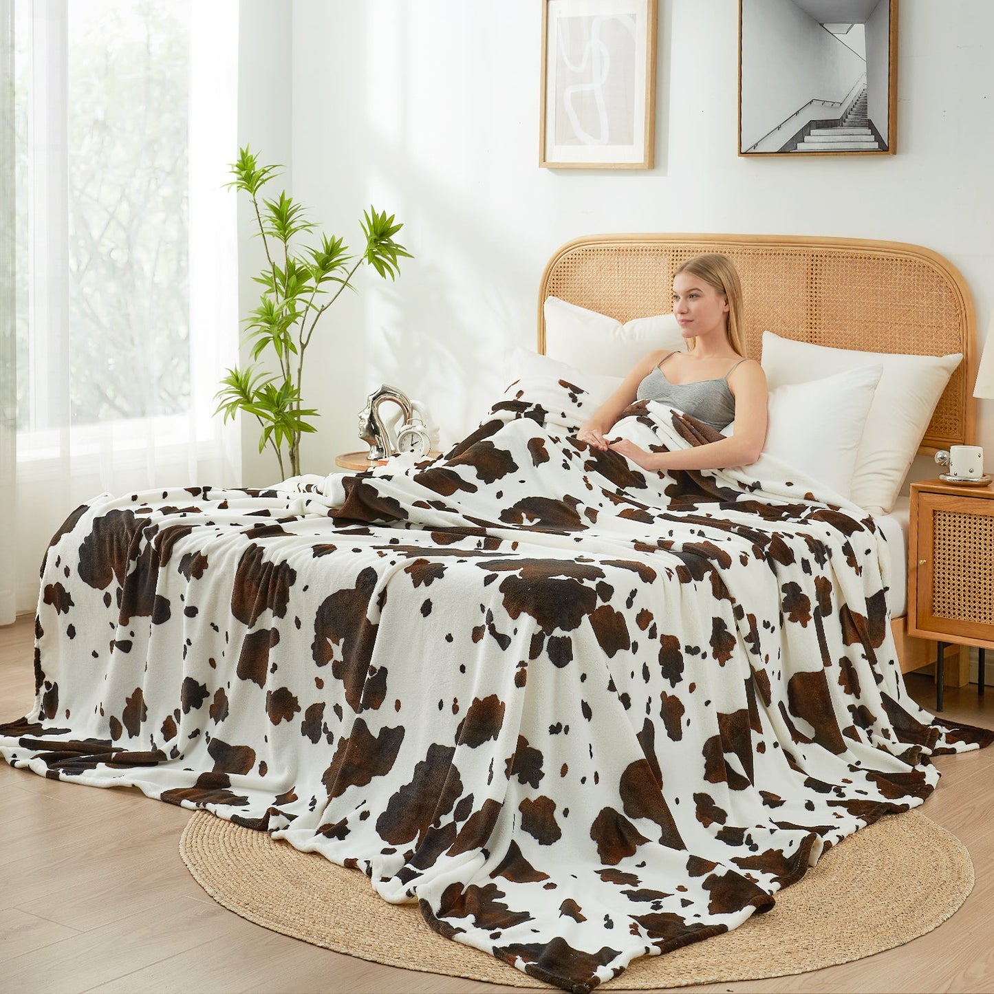 Woman sitting on a bed with a cow print blanket in a bright bedroom.