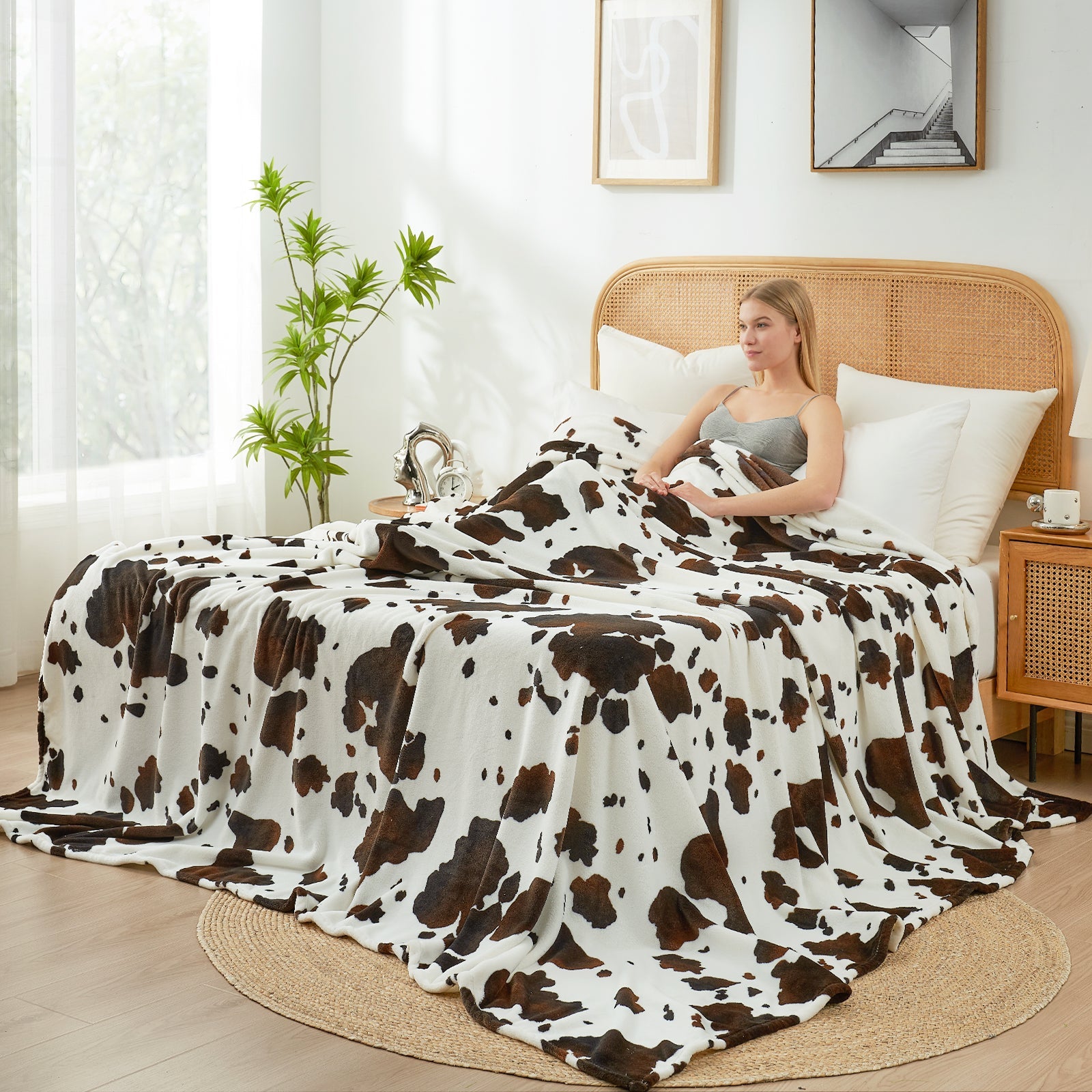 Woman sitting on a bed with a cow print blanket in a bright bedroom.