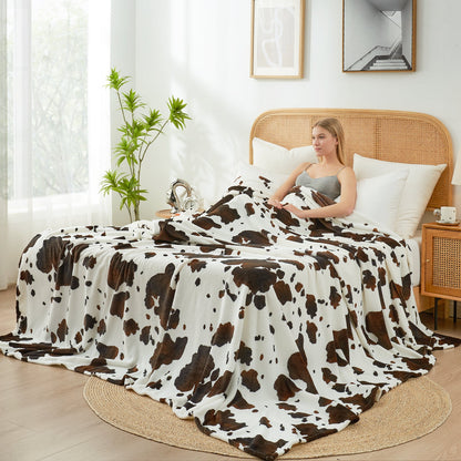 Woman sitting on a bed with a cow print blanket in a bright bedroom.