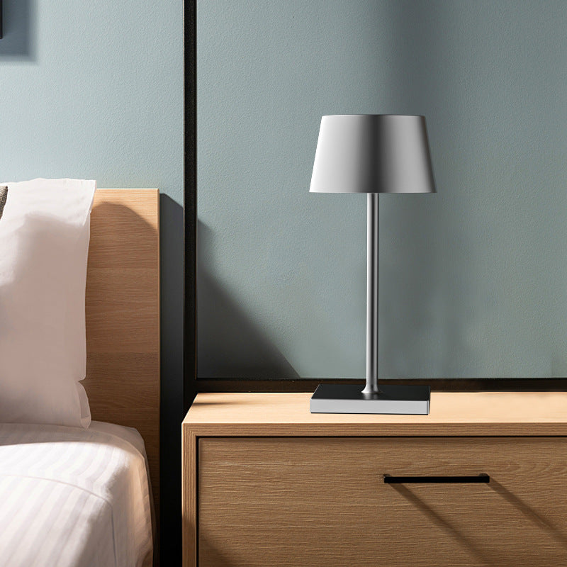 Table lamp on a wooden nightstand next to a bed with white bedding.