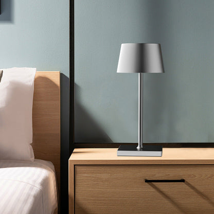 Table lamp on a wooden nightstand next to a bed with white bedding.