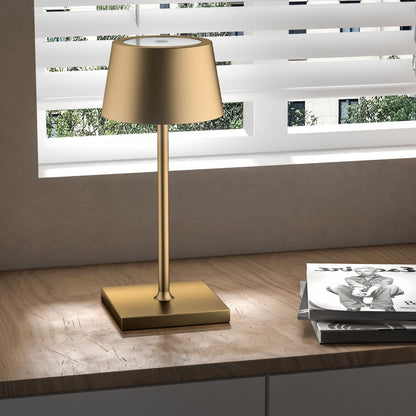 Gold table lamp on a wooden surface with a window in the background