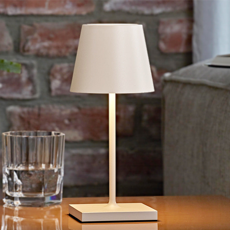 Table lamp with beige shade on a wooden surface in front of a brick wall.