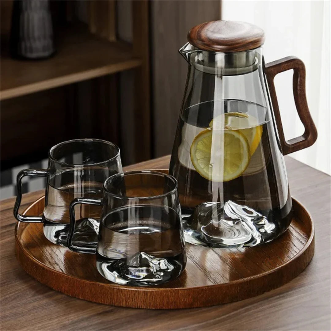 Josh & Tate - Montara Elegant Glass Pitcher - Clear glass carafe with wooden lid and handle, filled with lemon slices, on a wooden tray with three glasses.