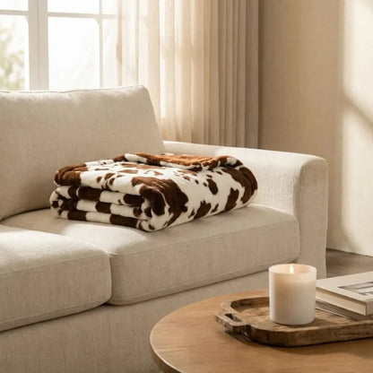 Josh & Tate MooWrap Cow Print Plush Blanket - folded on linen sofa in living room