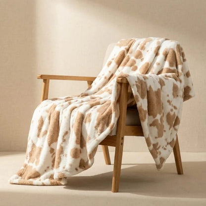 Josh & Tate MooWrap Cow Print Plush Blanket - khaki cow draped over armchair